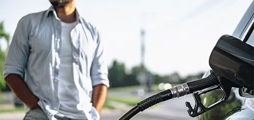 Señor en gasolinera cargando combustible a un auto gris.