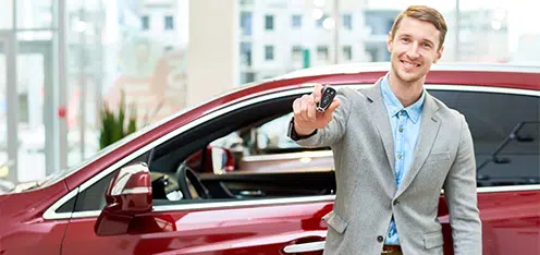 Señor vestido formal al lado de un carro rojo, mostrando el control de alarma del auto