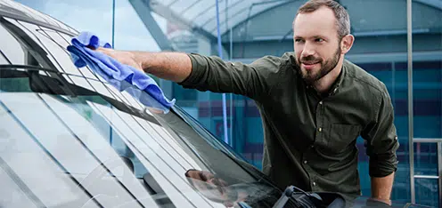 Señor camisa verde, limpiando con trapo azul el parabrisas de un auto