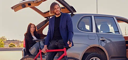 Mujer sentada al borde del baul de un carro y al lado un señor con una bicicleta roja.