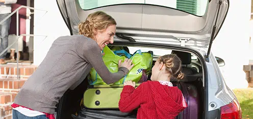 Mamá e hija, acomodando maletas en el baúl de un auto para viajar