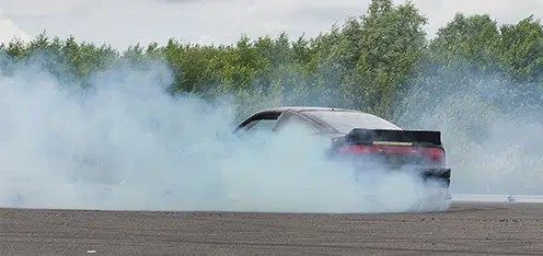 Auto negro con humo blanco del escape en una pista al aire libre